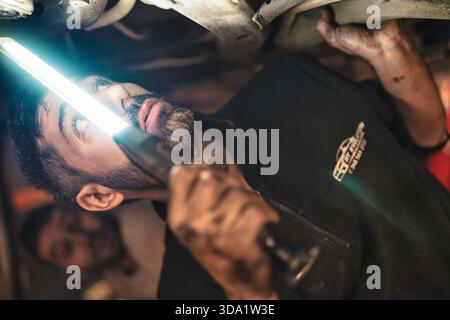 Rome, italie 20 novembre 2025 : mécanicien automobile inspectant le train de roulement de voiture dans le garage, tenant la lumière de travail brillante et axé sur l'entretien et la réparation di Banque D'Images