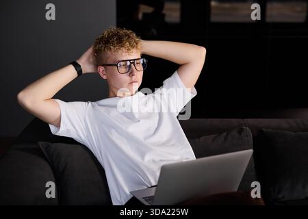 Jeune homme se relaxant tout en utilisant un ordinateur portable à la maison dans la soirée Banque D'Images