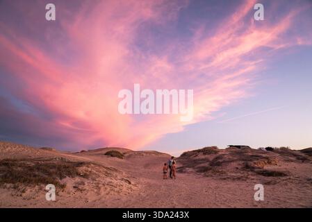 Une maman et deux enfants se tiennent dans des dunes de sable vides au coucher du soleil Banque D'Images