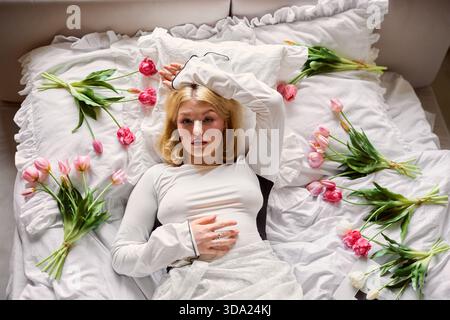Femme se reposant au lit avec des fleurs disposées autour d'elle sur les draps Banque D'Images