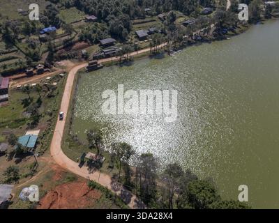 Vue aérienne paisible sur le lac, la route rurale et le village le jour ensoleillé. le paysage tranquille met en valeur l'eau sereine, la nature verdoyante et les paysages de campagne Banque D'Images