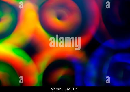 Image abstraite de formes de lumière circulaire tourbillonnantes floues dans les tons rouge, vert, bleu et jaune, se chevauchant sur un fond sombre avec des dégradés lisses, Banque D'Images