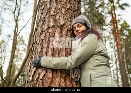 Femme embrassant l'arbre. Aimez la nature et la terre. Forêt d'hiver. Méditation consciente. Pleine conscience et mise à la terre. Calme zen santé mentale. Énergie extérieure. Banque D'Images