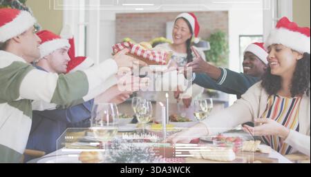 Amis de passage échangeant panier-cadeau emballé à la salle à manger à la maison, portant des chapeaux de Père Noël Banque D'Images