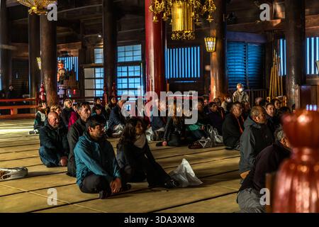 Pèlerins et visiteurs sont assis sur des tatamis dans le grand hall principal (Hondo) du temple Zenkoji à Nagano et assistent à la cérémonie du matin. La salle est considérée comme l'un des plus grands temples en bois du Japon ; Zenkoji est ouvert aux personnes de toutes les confessions et attire les croyants de toutes les écoles bouddhistes. Nagano, Préfecture de Nagano, Japon Banque D'Images