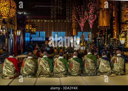 Une vue en grand angle d'une cérémonie bouddhiste au temple Zenkoji à Nagano : une rangée complète de moines en kesa brodé d'or s'assoit sur des tatamis devant l'autel principal, tandis qu'un batteur en arrière-plan accompagne rythmiquement la liturgie. Zenkoji est interconfessionnel et abrite des prêtres des écoles Tendai et Jōdo. Nagano, Préfecture de Nagano, Japon Banque D'Images