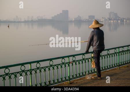 Un pêcheur vietnamien solitaire portant un chapeau conique au lac brumeux de l'Ouest, Hanoi, Vietnam Banque D'Images
