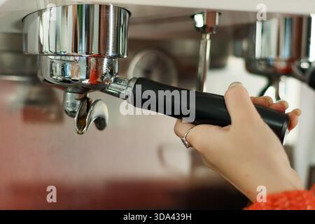Vue rapprochée des doigts fixant la poignée noire sur la machine espresso lorsque le liquide s'écoule. Banque D'Images