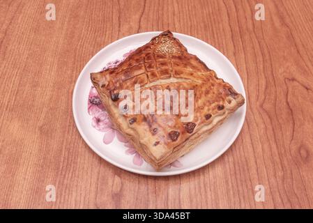 Tarte aux pommes dans une coquille de pâte feuilletée avec de fines tranches de pomme disposées en forme de rose, saupoudrées de sucre en poudre et servies avec une cuillère de van Banque D'Images