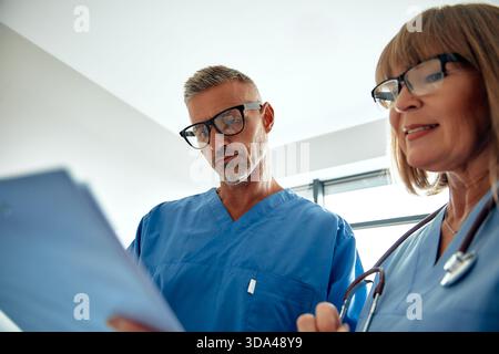 Dans une conversation significative, deux fournisseurs de soins de santé échangent des informations vitales sur les patients, soulignant le rôle crucial du travail d’équipe et de la collaboration Banque D'Images