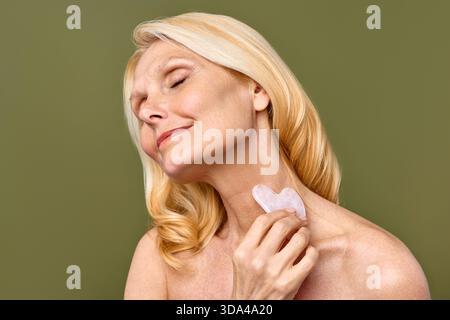 Une femme met en valeur de manière experte l'utilisation efficace d'un outil gua Sha pour les soins de la peau et la promotion du bien-être du visage, le tout sur un fond vert apaisant Banque D'Images