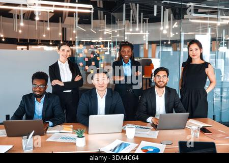 Équipe de jeunes travailleurs d'affaires réussis dans des costumes formels avec des ordinateurs portables dans un bureau moderne. Des jeunes de différentes nationalités travaillant en coworkin Banque D'Images