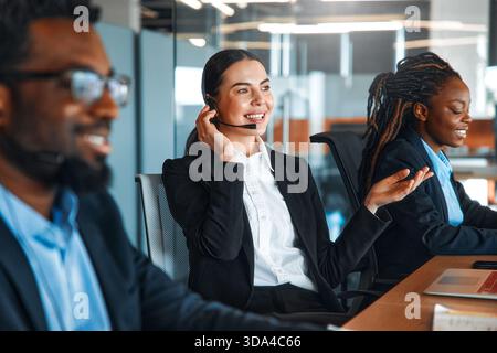 Équipe d'employés de centre d'appels performants avec des micro-casques assis avec des ordinateurs portables à table et répondant aux appels, fournissant assistance et assistance au client Banque D'Images