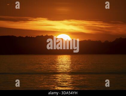 Le soleil se couche derrière les sommets des montagnes, vue sur Cook Inlet au coucher du soleil, lumière dorée pittoresque du soleil de minuit, montagnes de la chaîne des Aléoutiennes, Anchor po Banque D'Images