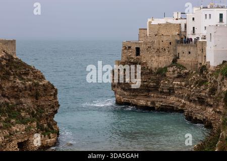 bâtiments historiques blancs perchés dramatiquement au sommet d'une falaise de calcaire accidentée surplombant la mer adriatique turquoise à polignano a mare, pouilles, italie, Banque D'Images