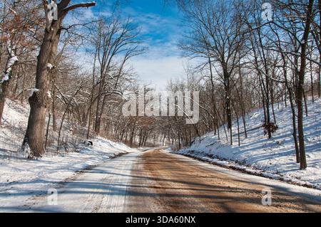 Snow-covered road cutting through wooded hills in the Lower Kettle Moraine near Palmyra, Wisconsin, in winter. Banque D'Images