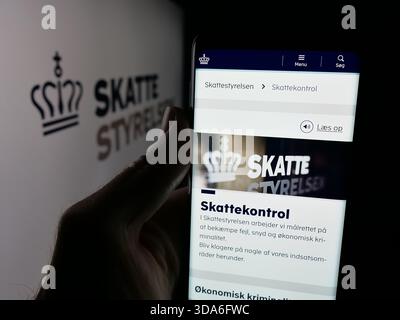 Dans cette illustration photo, une personne tient un téléphone portable avec la page Web de l'agence fiscale danoise Skattestyrelsen sur l'écran devant le logo. Banque D'Images