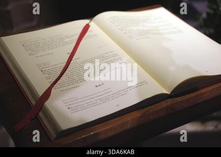 Vue large du livre liturgique ouvert en langue polonaise placé sur un pupitre en bois foncé, des pages de papier crème avec du texte noir et rouge, signet ruban rouge. Banque D'Images