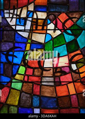 Gros plan de vitrail composé de segments de verre géométriques irréguliers en bleu, rouge, vert, jaune, orange, blanc et violet. Banque D'Images