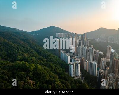 Vue aérienne de gratte-ciel denses juxtaposés à des montagnes verdoyantes sous un ciel doux et doré, Hong Kong Island, Hong Kong Island, Hong Kong Island. Banque D'Images