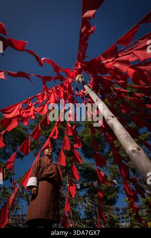 Vue de drapeaux de prière rouges vibrants flottant autour d'un poteau en bois sous un ciel bleu profond, contrastant avec les arbres verts du col de Kikila, Bumthang, Banque D'Images