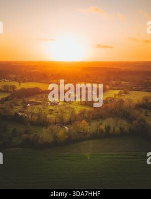 Vue aérienne du soleil plongeant sous l'horizon, peignant le ciel avec des teintes d'orange et d'or sur le paysage serein, Saint-Hymer, Normandie, Fran Banque D'Images