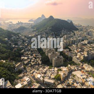 Vue aérienne d'un paysage urbain dynamique mêlant bâtiments modernes et favelas sur fond de montagnes verdoyantes et d'océan lointain, Rio de Janeiro, St. Banque D'Images