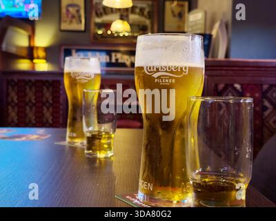 Une photo de deux pintes de Carlsberg Pils lager partiellement ivre accompagné de verres de whisky sur une table de pub irlandais Banque D'Images