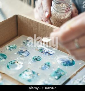 Mains fabriquant des bijoux en résine colorés à l'aide de moules et d'embellissements. Banque D'Images