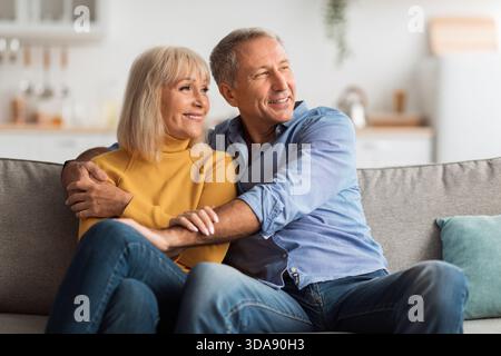 Joyeux couple profite d'un moment confortable ensemble à la maison tout en se relaxant sur le canapé dans un espace de vie lumineux Banque D'Images