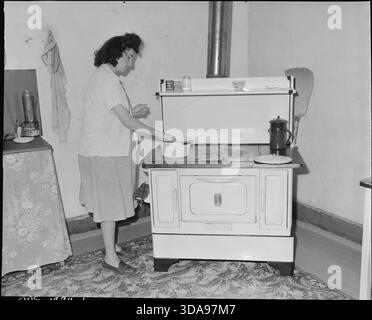 Cette photographie représente MRS Paul May, la femme d'un mineur, dans la cuisine de sa maison de quatre pièces à Jewell, probablement pendant la Grande dépression. Son ménage manque d’eau courante, ce qui illustre les mauvaises conditions de vie des familles ouvrières tributaires des revenus miniers. L’image met en lumière le travail domestique, la pauvreté rurale et les difficultés des familles des mineurs en Amérique du début du XXe siècle. Banque D'Images