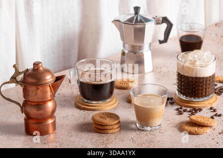 Expresso fraîchement infusé, café glacé et deux pots à moka dans une cuisine beige confortable. Différents types de boissons au café avec des biscuits sur une table beige Banque D'Images