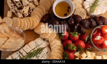 Belle planche de charcuterie avec fromages assortis, fruits frais, dattes et poivrons farcis au fromage à la crème. Parfait pour le partage, les fêtes ou l'application élégante Banque D'Images