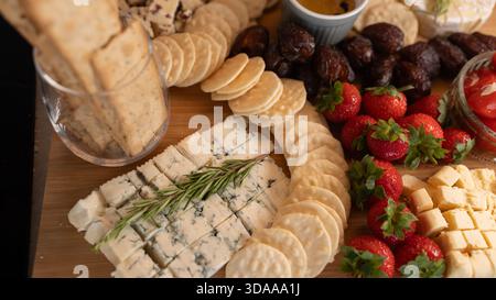 Belle planche de charcuterie avec fromages assortis, fruits frais, dattes et poivrons farcis au fromage à la crème. Parfait pour le partage, les fêtes ou l'application élégante Banque D'Images