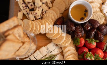 Belle planche de charcuterie avec fromages assortis, fruits frais, dattes et poivrons farcis au fromage à la crème. Parfait pour le partage, les fêtes ou l'application élégante Banque D'Images