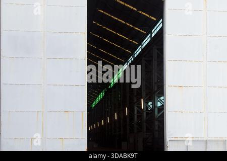 L'intérieur sombre d'un immense entrepôt, vu entre deux portes métalliques coulissantes géantes. La seule lumière entrant dans le bâtiment provient de minuscules fenêtres Banque D'Images