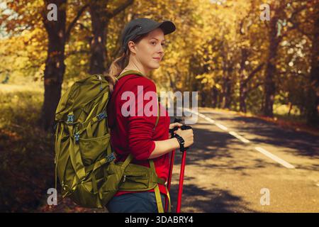 Jeune femme balades touristiques avec des bâtons et sac à dos sur route à l'automne Banque D'Images