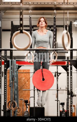 La formation d'athlète de femme a pesé le muscle vers le haut sur les anneaux de gymnastique dans un gymnase de fitness moderne Banque D'Images
