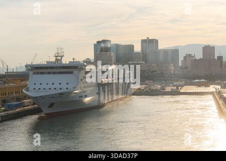 06.18.25, Genua, Italie, grand ferry de croisière blanc entrant dans le port au lever du soleil. La lumière dorée chaude se reflète sur l'eau, avec les bâtiments de la ville et Banque D'Images