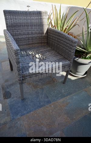 Une chaise en osier extérieure usée avec un siège cassé se trouve sur un patio en pierre sous la lumière naturelle du soleil. Banque D'Images