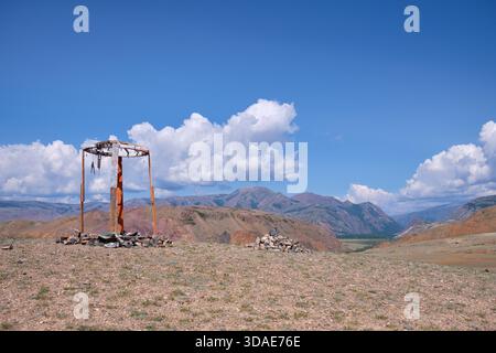 Construction religieuse en bois dans les montagnes de l'Altaï. Fait de poteaux et de pierres en bois. En arrière-plan chaîne de montagnes Kurai sous ciel bleu et nuages. Banque D'Images