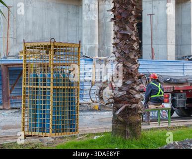 Bouteilles de gaz dans la cage de sécurité près de Palm Tree et ouvrier de construction sur le chantier Banque D'Images