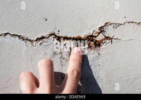 Personne inspectant une fissure dans le mur avec de l'eau qui s'échappe. Gros plan de la main examinant la fissure verticale dans le mur extérieur avec rouille et efflorescence. Réparation Banque D'Images