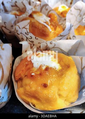 Vue rapprochée verticale de muffins dorés fraîchement cuits servis dans d'élégantes tulipes en papier à motifs. Les pâtisseries humides sont recouvertes d'un gl Banque D'Images