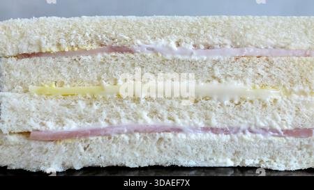 Vue latérale détaillée d'un sandwich club maison composé de trois couches de pain blanc moelleux et sans croûte. La garniture se compose de jambon tranché, cheddar ch Banque D'Images