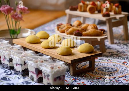 Une table sucrée avec des gâteaux aux baies jaunes et des pâtisseries orientales au buffet. Desserts mochi et trifle dans des récipients en plastique sur un t magnifiquement mis Banque D'Images