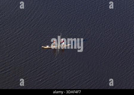 Aérien de deux pêcheurs debout sur un mokoro et mettant dans quelques filets par une chaude soirée dans le delta de l'Okavango au Botswana Banque D'Images