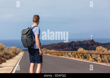 Randonneur avec sac à dos tourne sur la route côtière vers le phare sur Tenerife. La scène montre le moment de voyage calme dans le paysage lumineux de l'île avec l'atmosphe de l'océan Banque D'Images