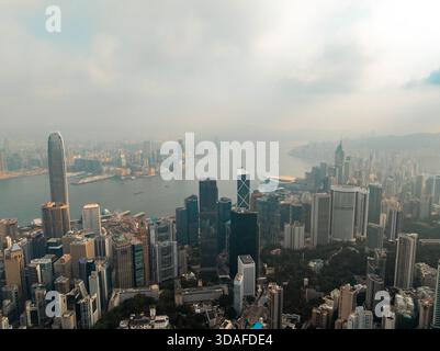Vue aérienne de gratte-ciel traversant la brume, juxtaposés aux eaux scintillantes du port Victoria et aux parcs verdoyants, Hong Kong, Hong Ko Banque D'Images