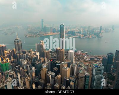 Vue aérienne de gratte-ciel traversant la ligne d'horizon brumeuse, juxtaposée aux eaux chatoyantes du port Victoria, île de Hong Kong, Hong Kon Banque D'Images